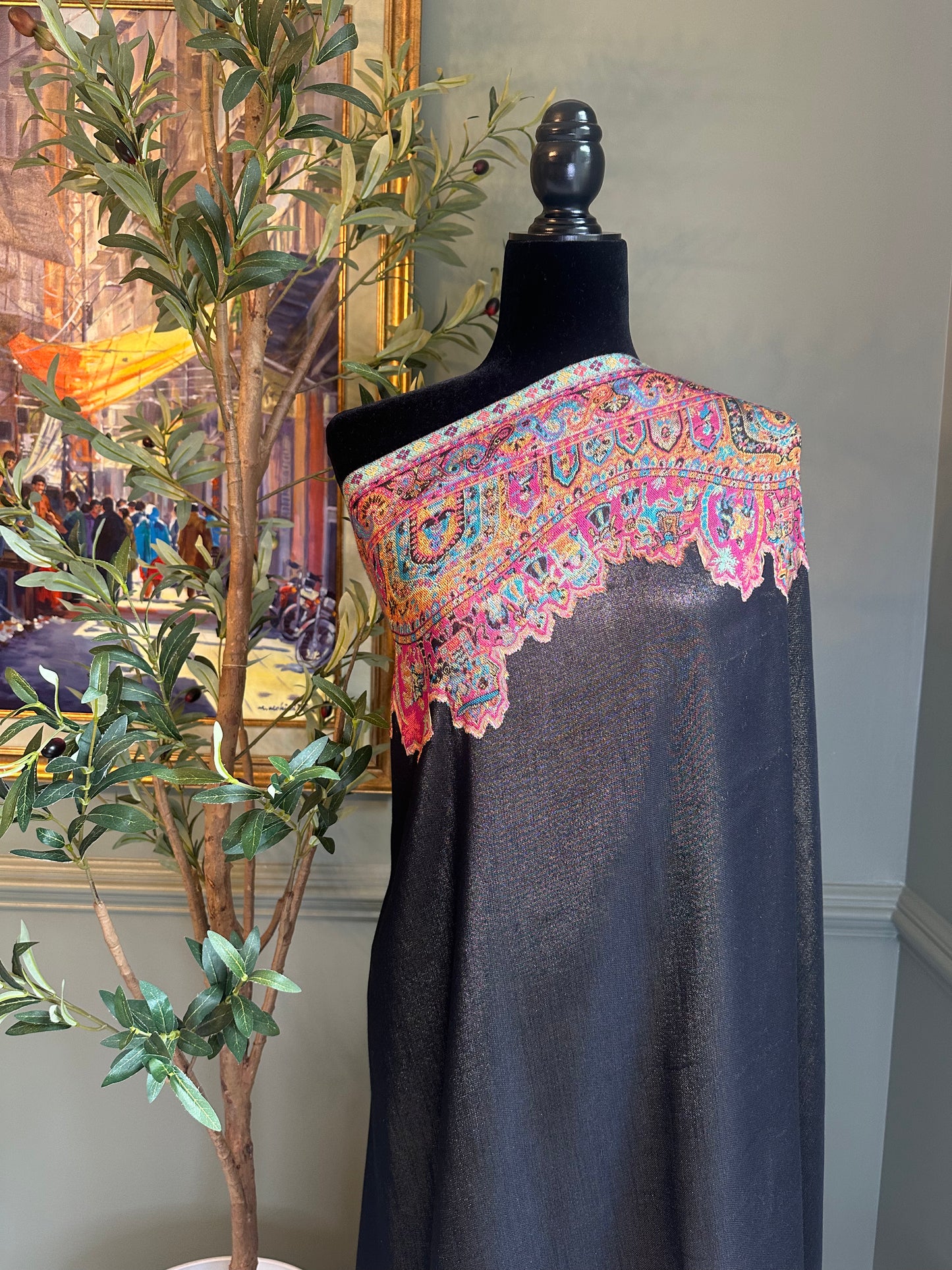 Mannequin wearing a dark fabric with colorful embroidered shoulder piece in a room setting.
