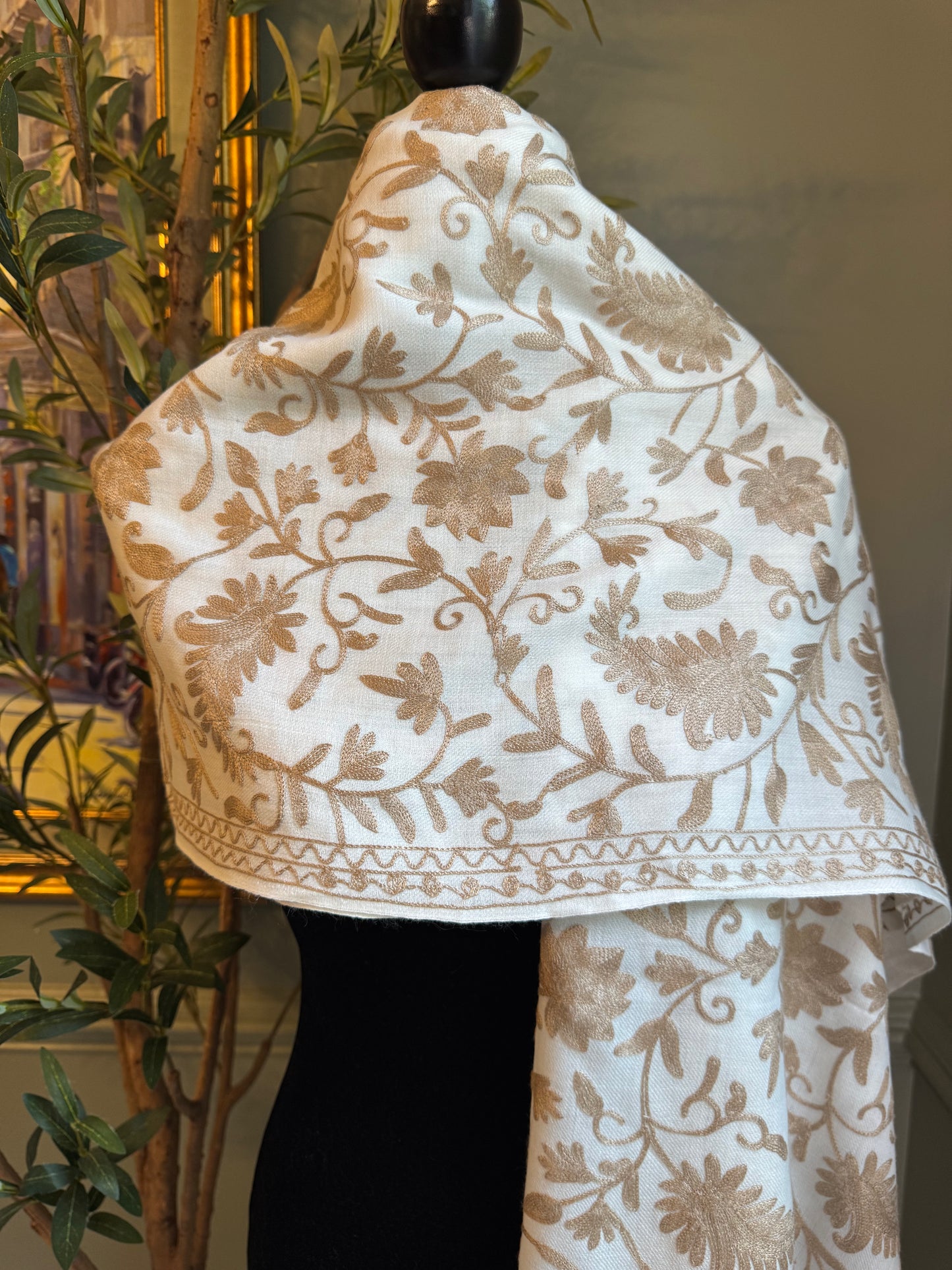 White fabric with beige floral patterns draped over a black object, with a plant in the background.