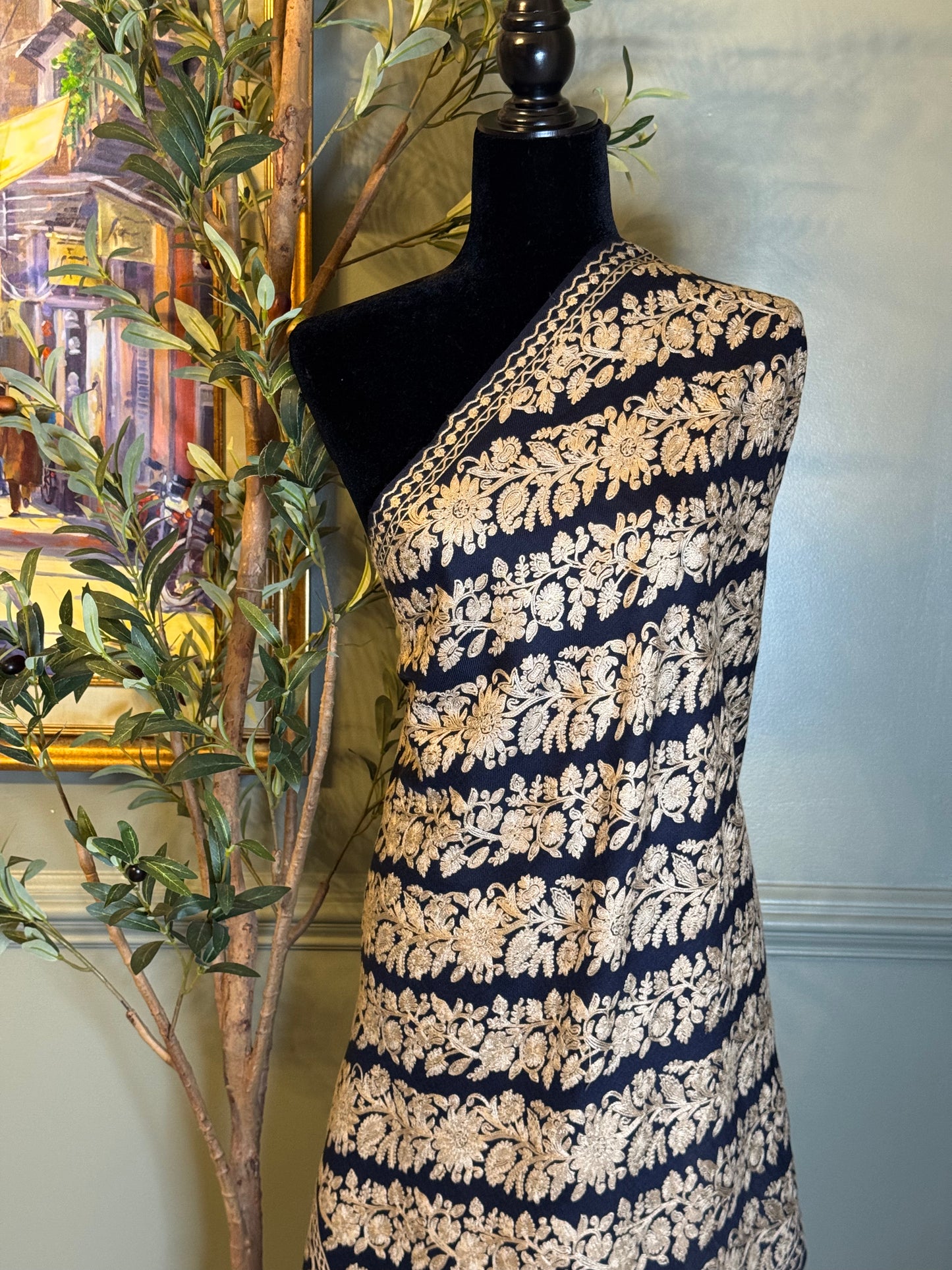 Mannequin wearing a navy and gold patterned shawl against a neutral wall.