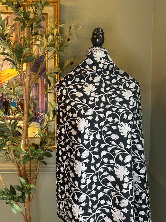 Mannequin draped with a black and white floral patterned fabric against a neutral wall.