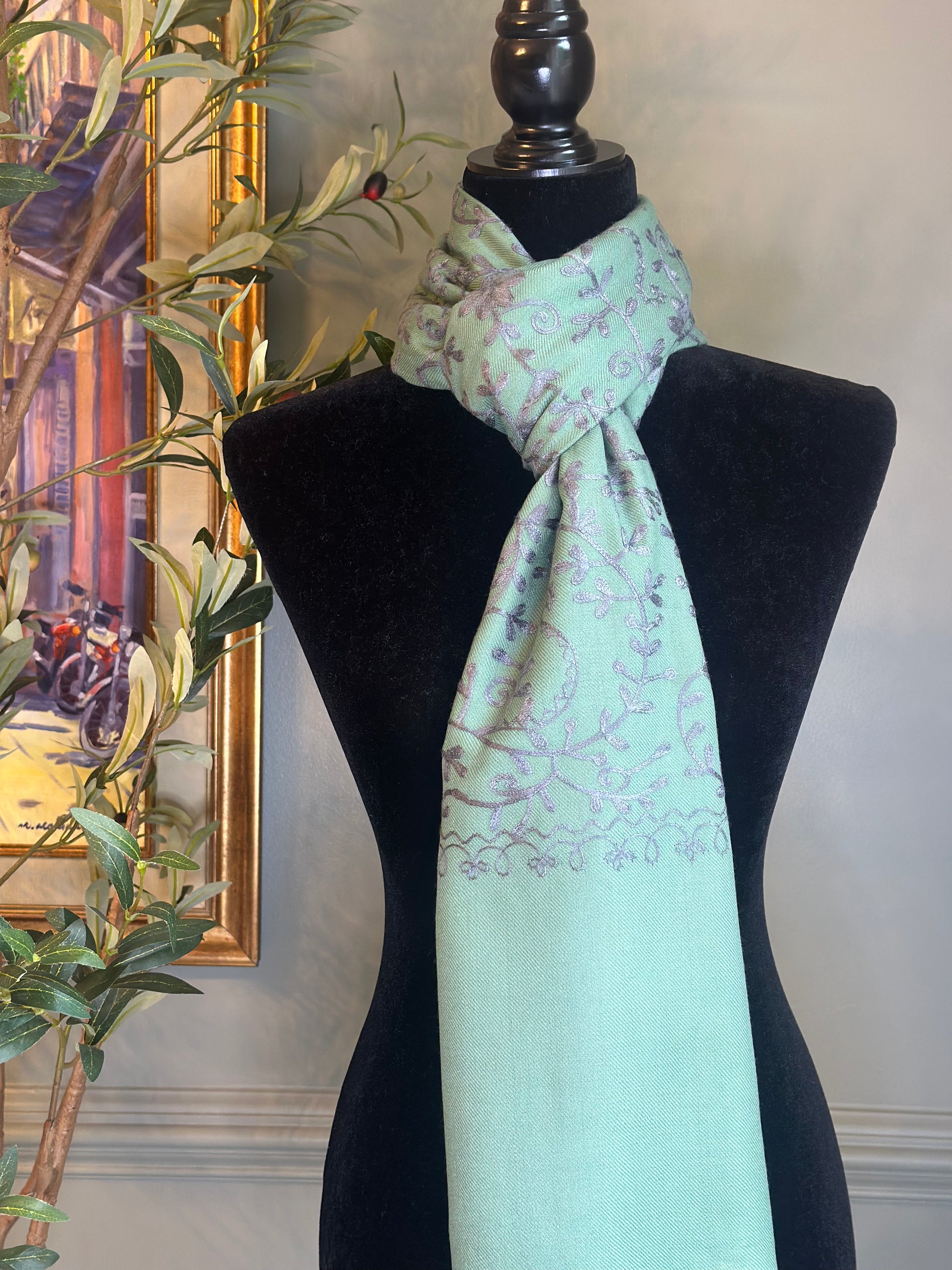 Mint green scarf with floral pattern on a black mannequin against a neutral wall.