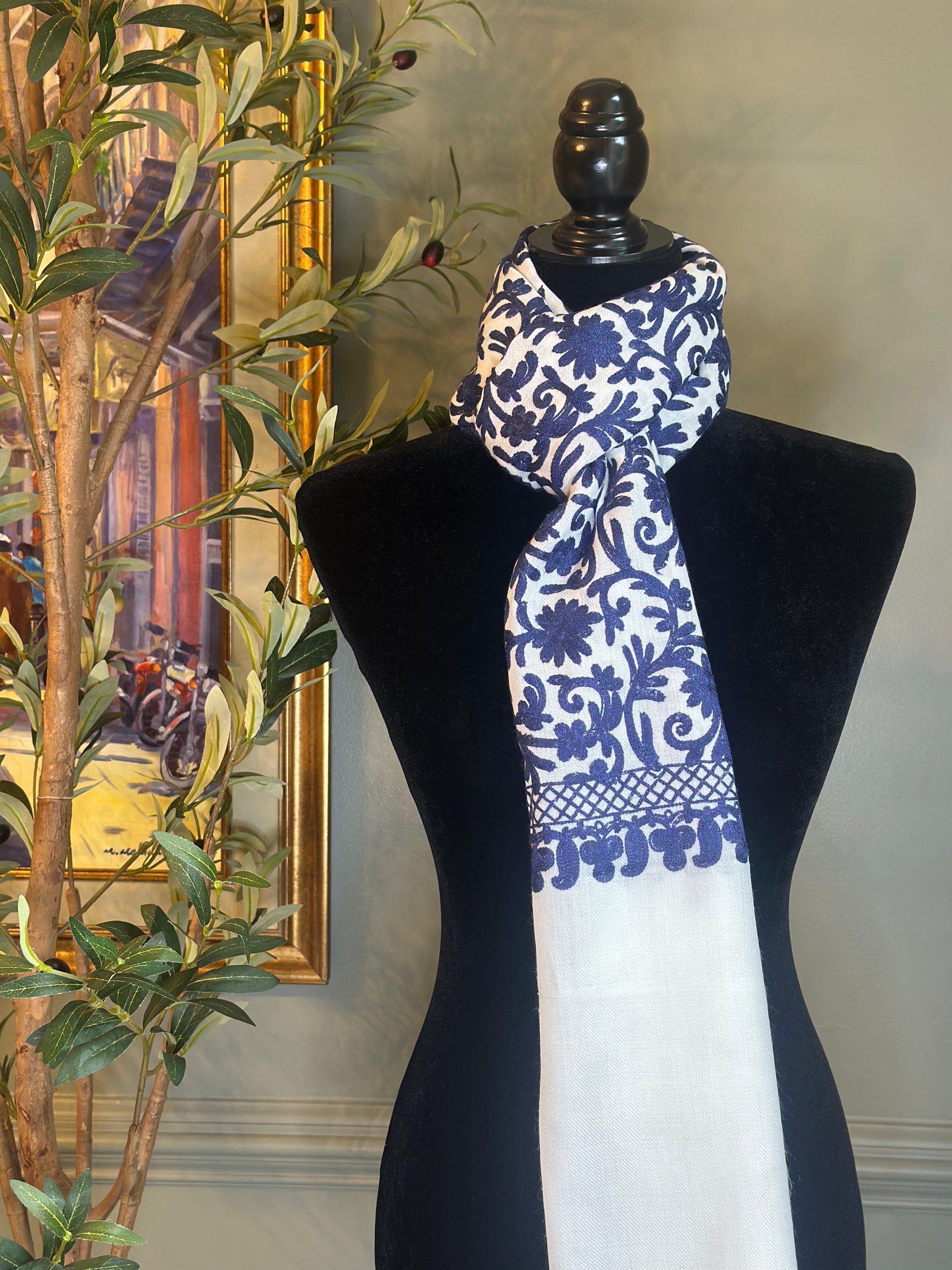 White scarf with blue floral pattern draped over a black mannequin against a neutral wall.