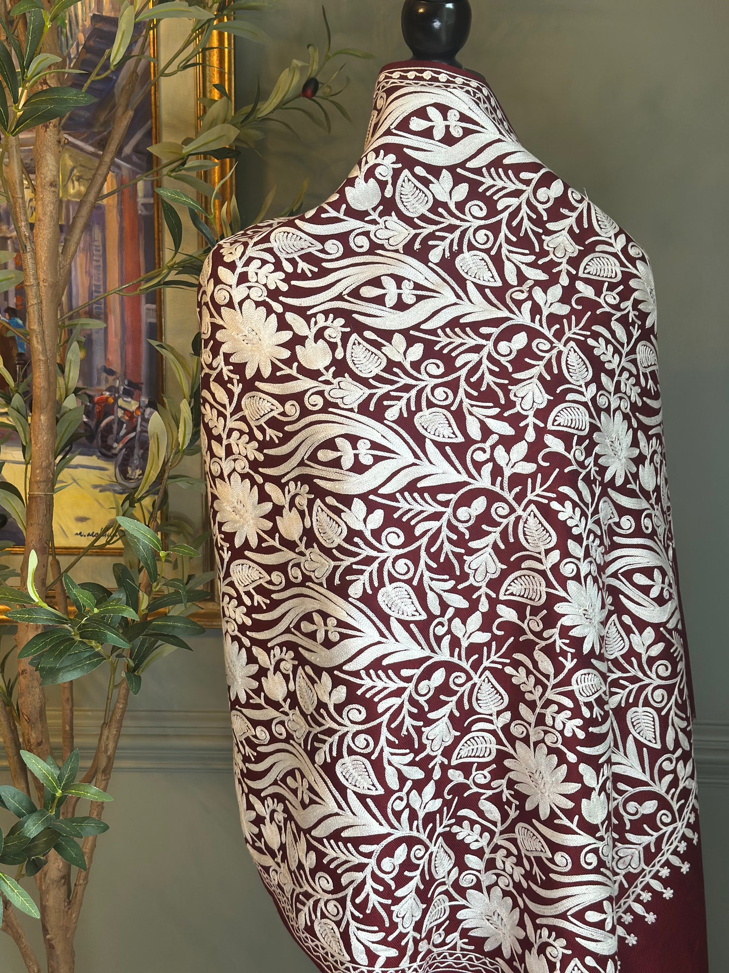 Mannequin wearing a patterned garment with a plant and framed picture in the background
