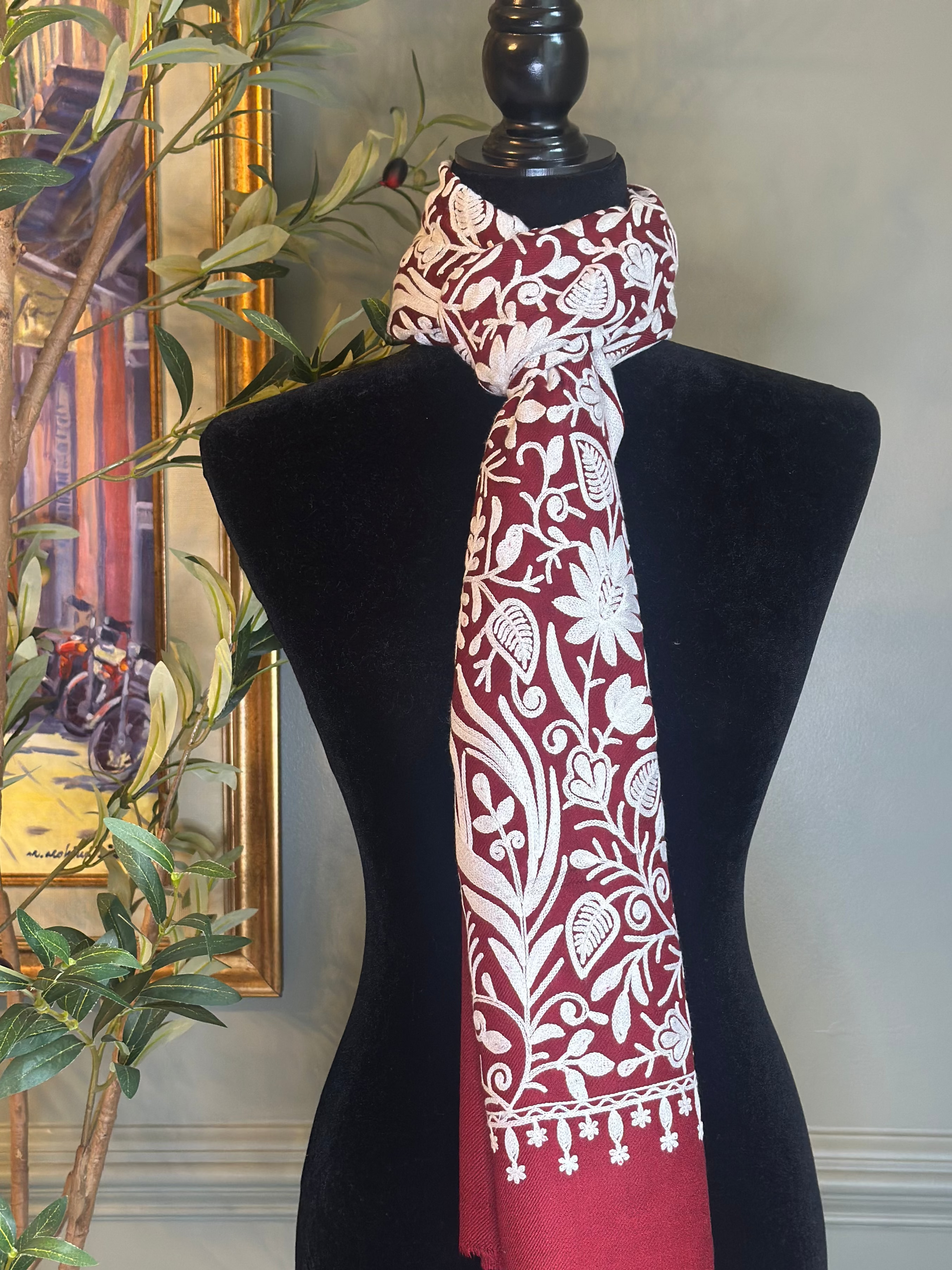 Red and white patterned scarf on a black mannequin against a neutral wall.