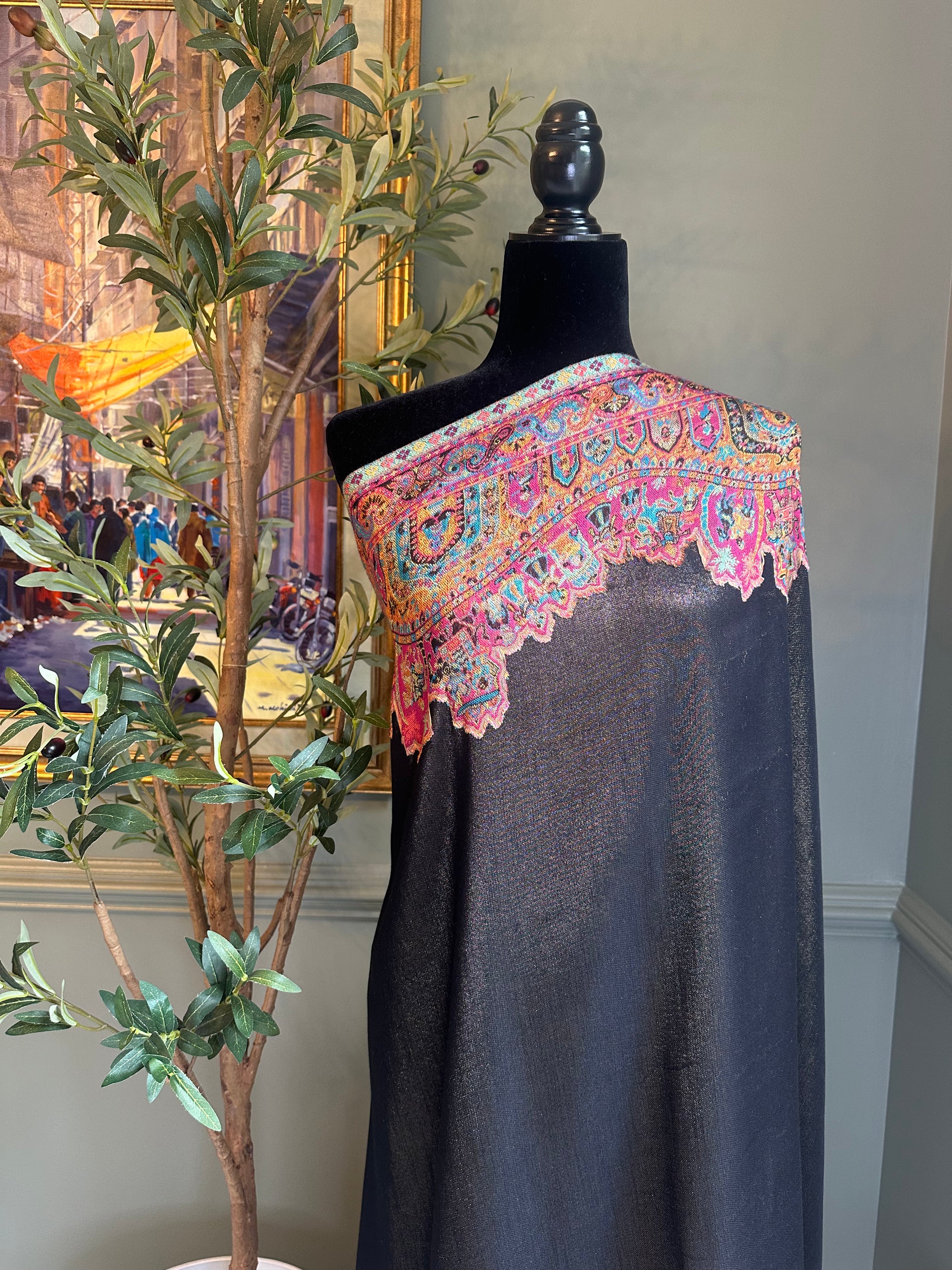 Mannequin wearing a dark fabric with colorful embroidered shoulder piece in a room setting.