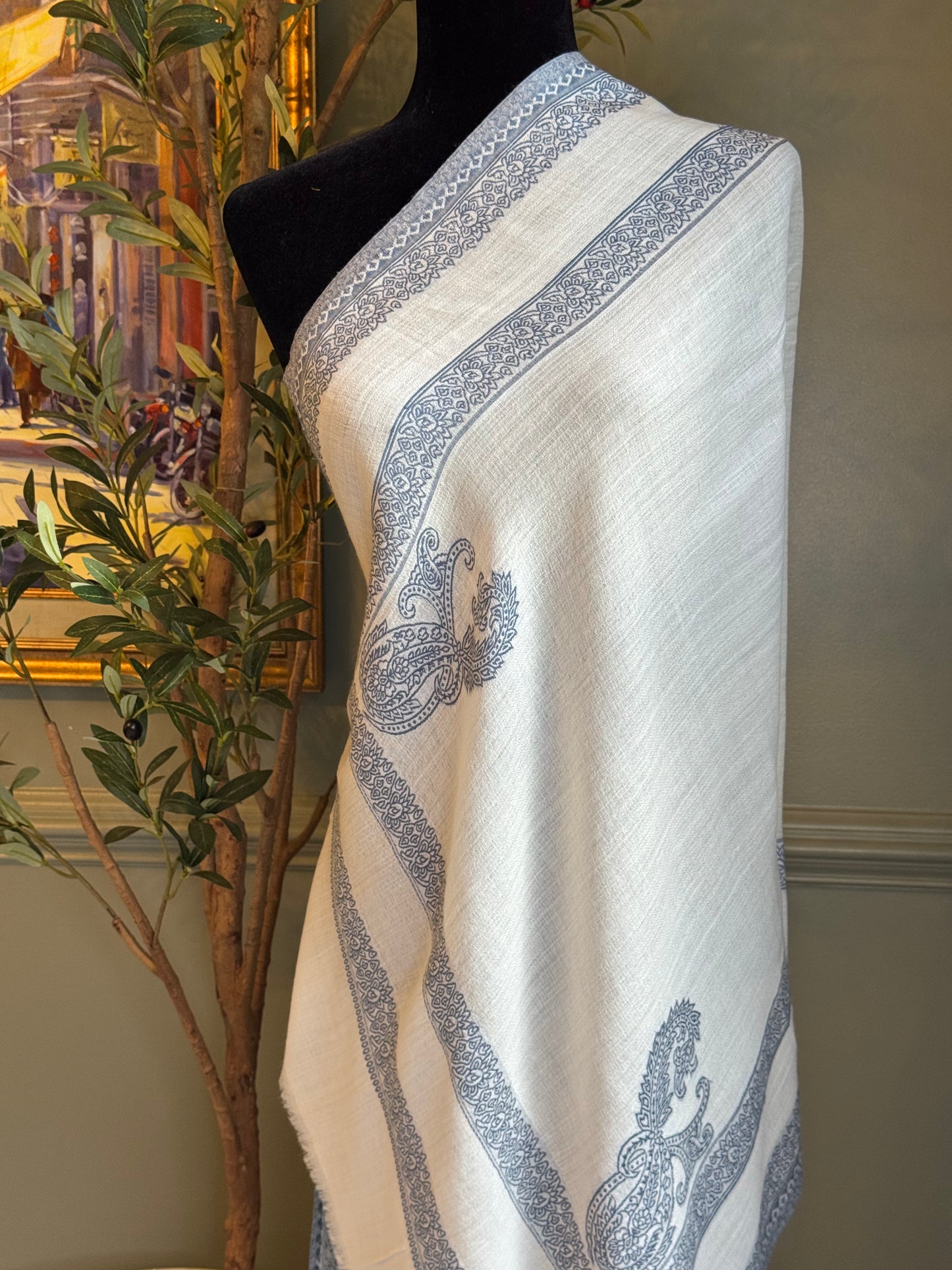 White scarf with blue patterns draped over a mannequin against a neutral wall.