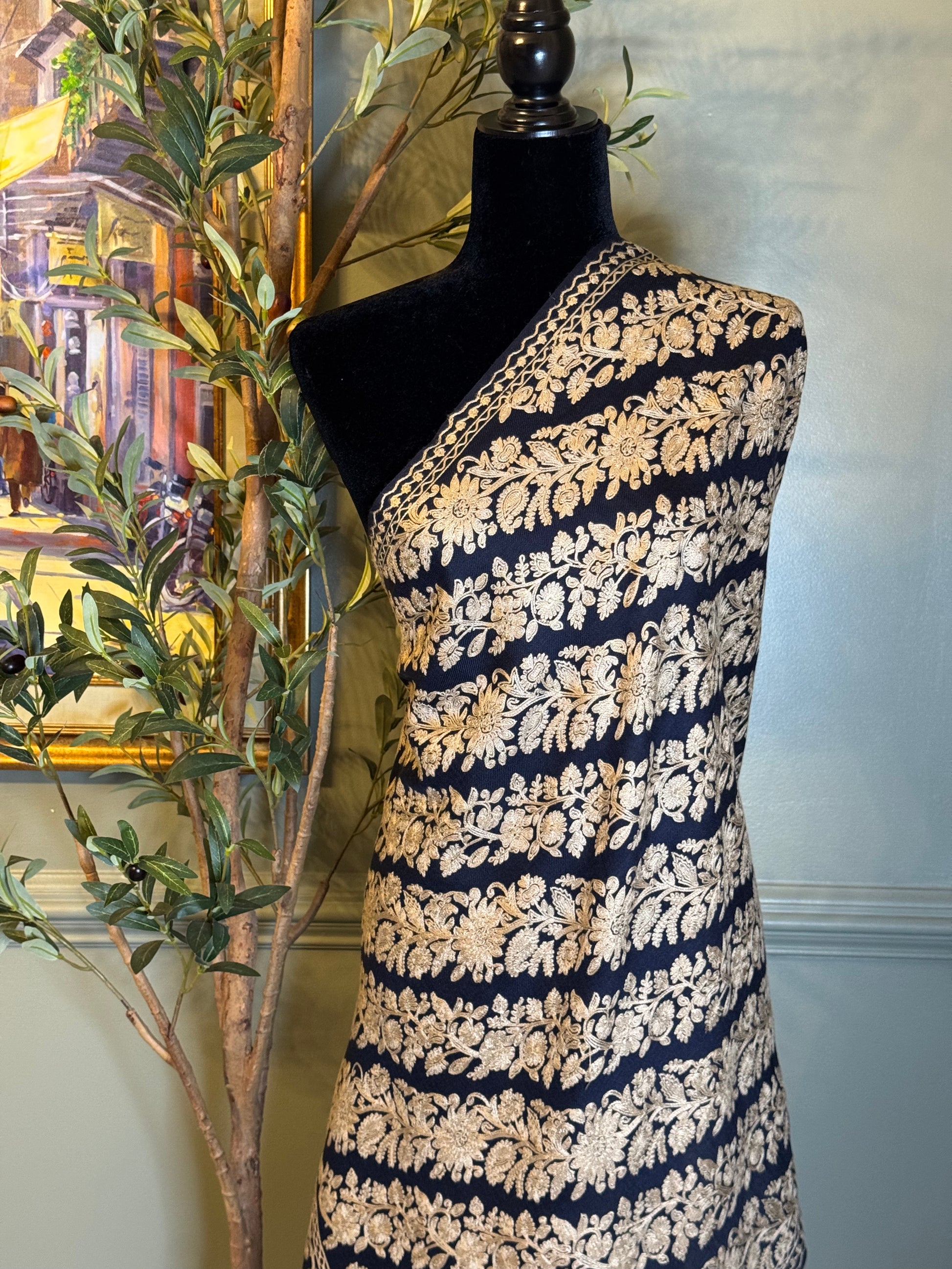 Mannequin wearing a navy and gold patterned shawl against a neutral wall.