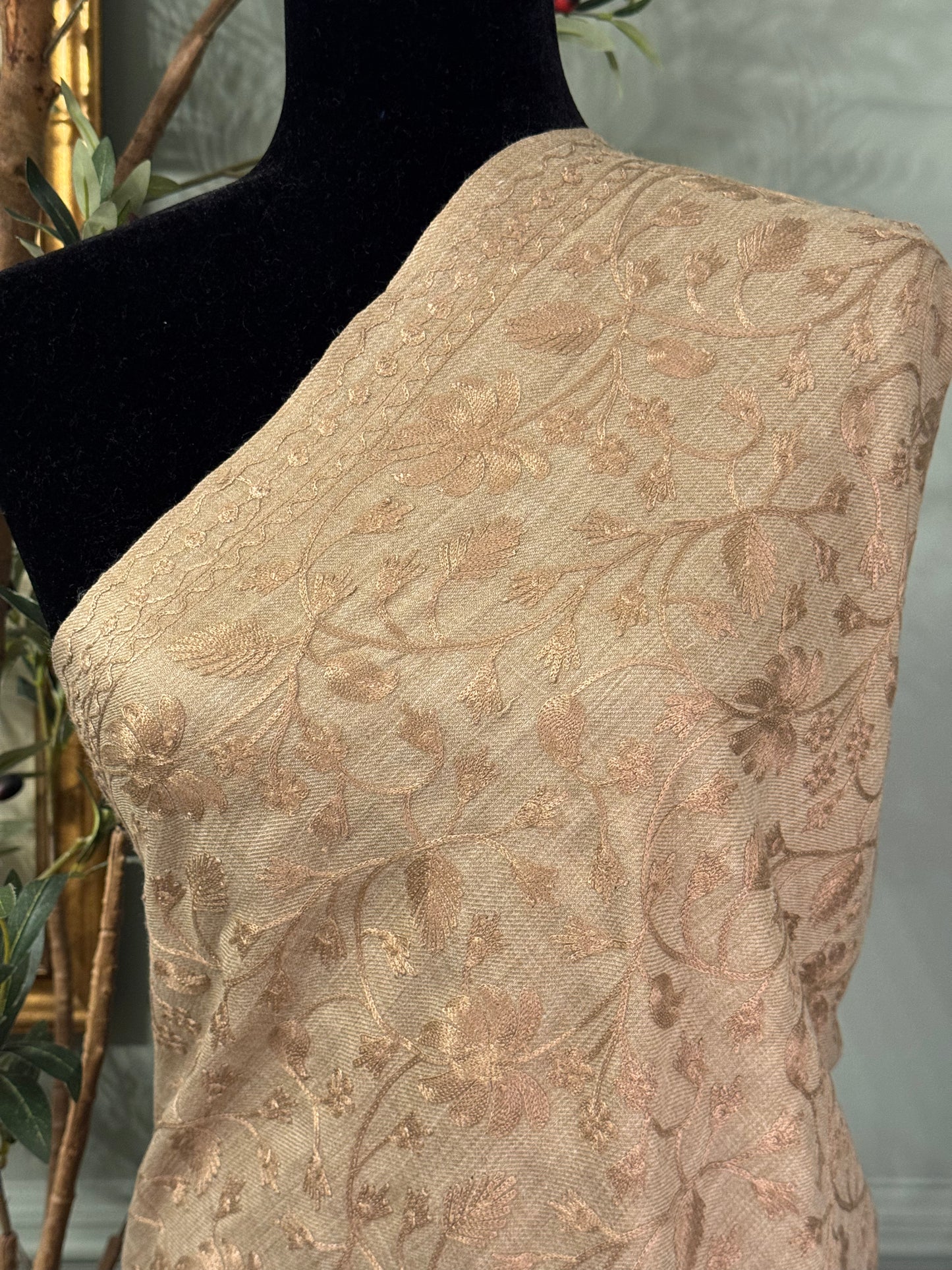 Beige fabric with floral embroidery on a mannequin against a neutral background