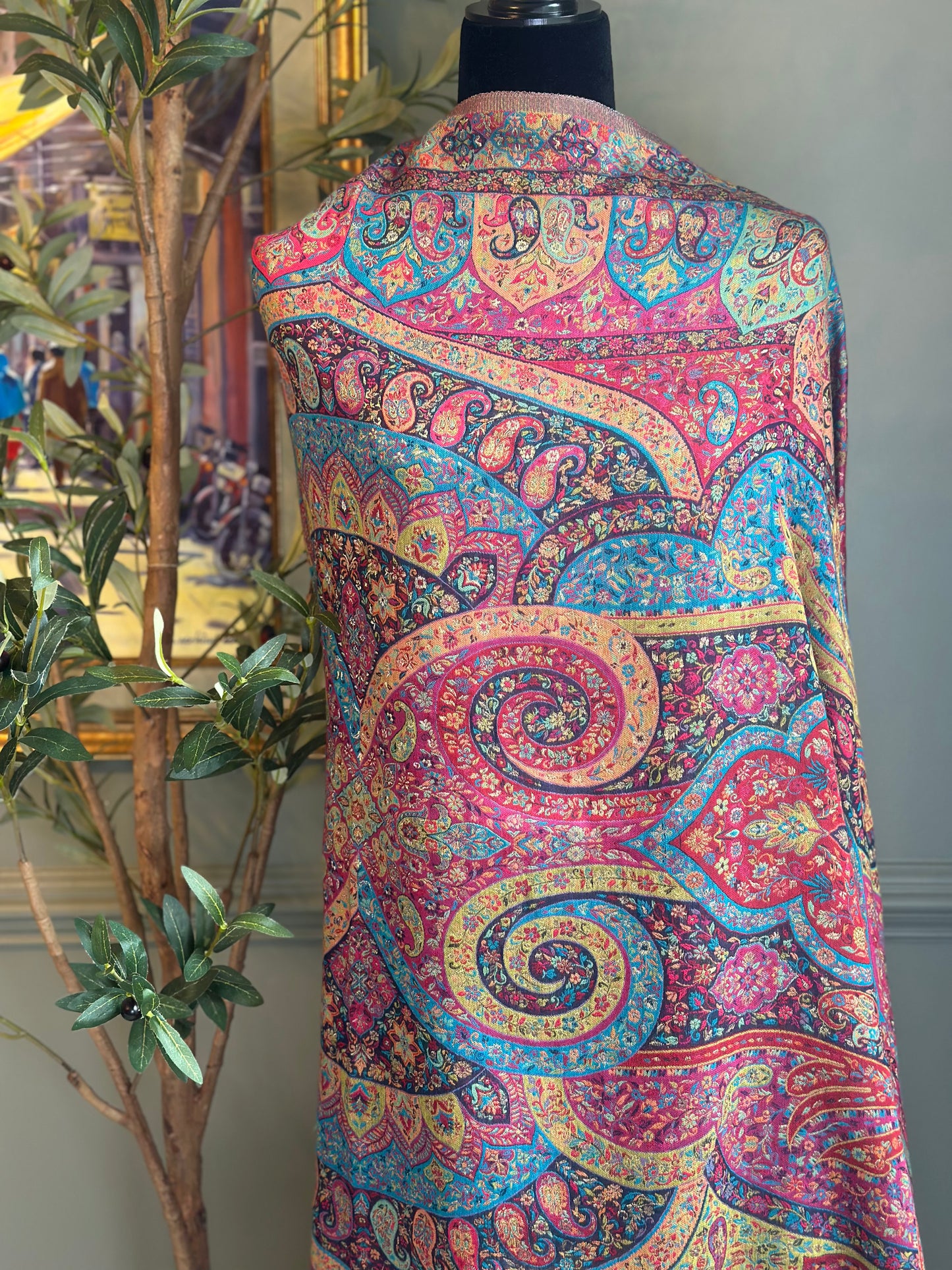 Colorful paisley-patterned vest on a mannequin with a plant and framed picture in the background