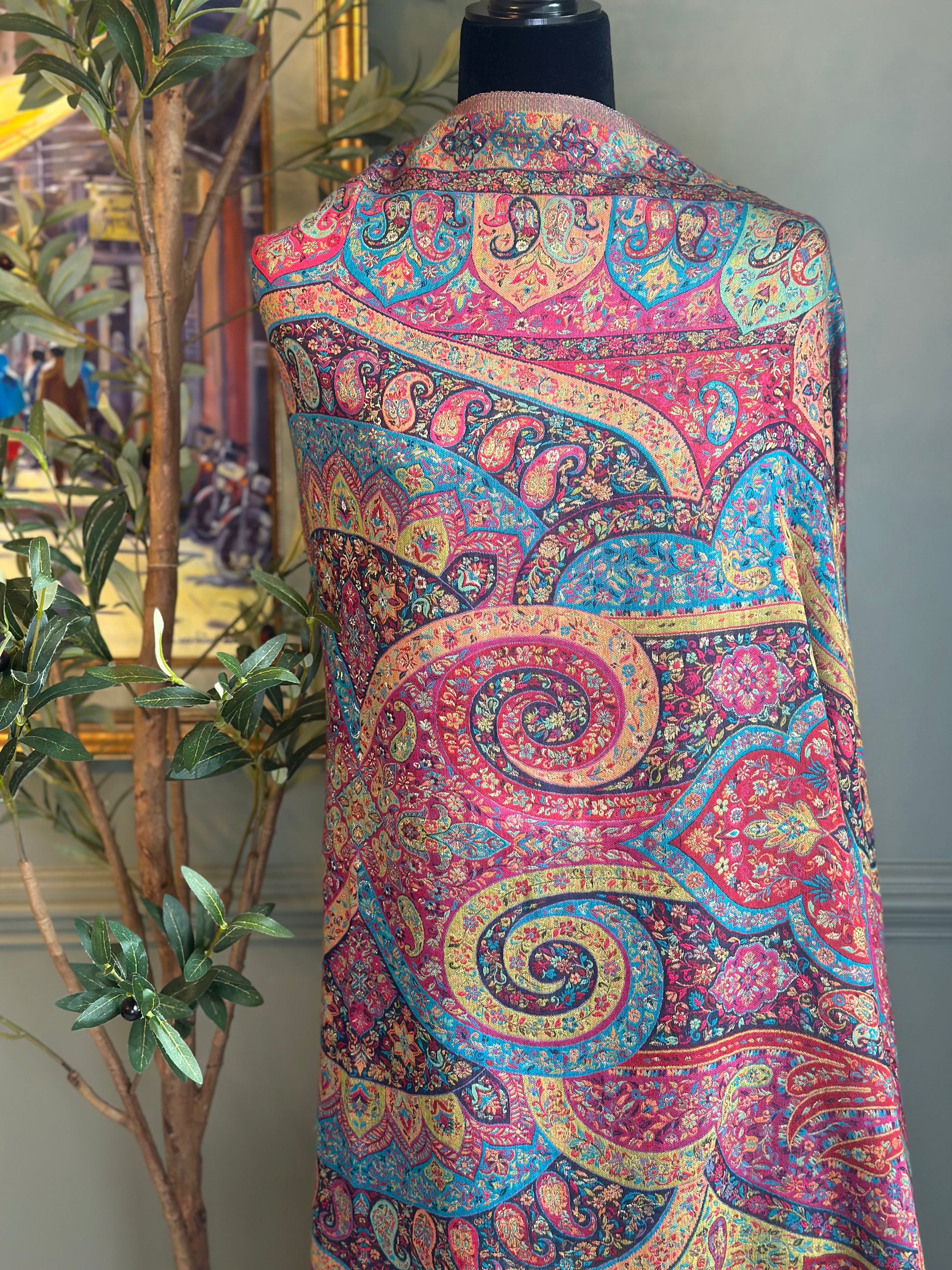 Colorful paisley-patterned vest on a mannequin with a plant and framed picture in the background