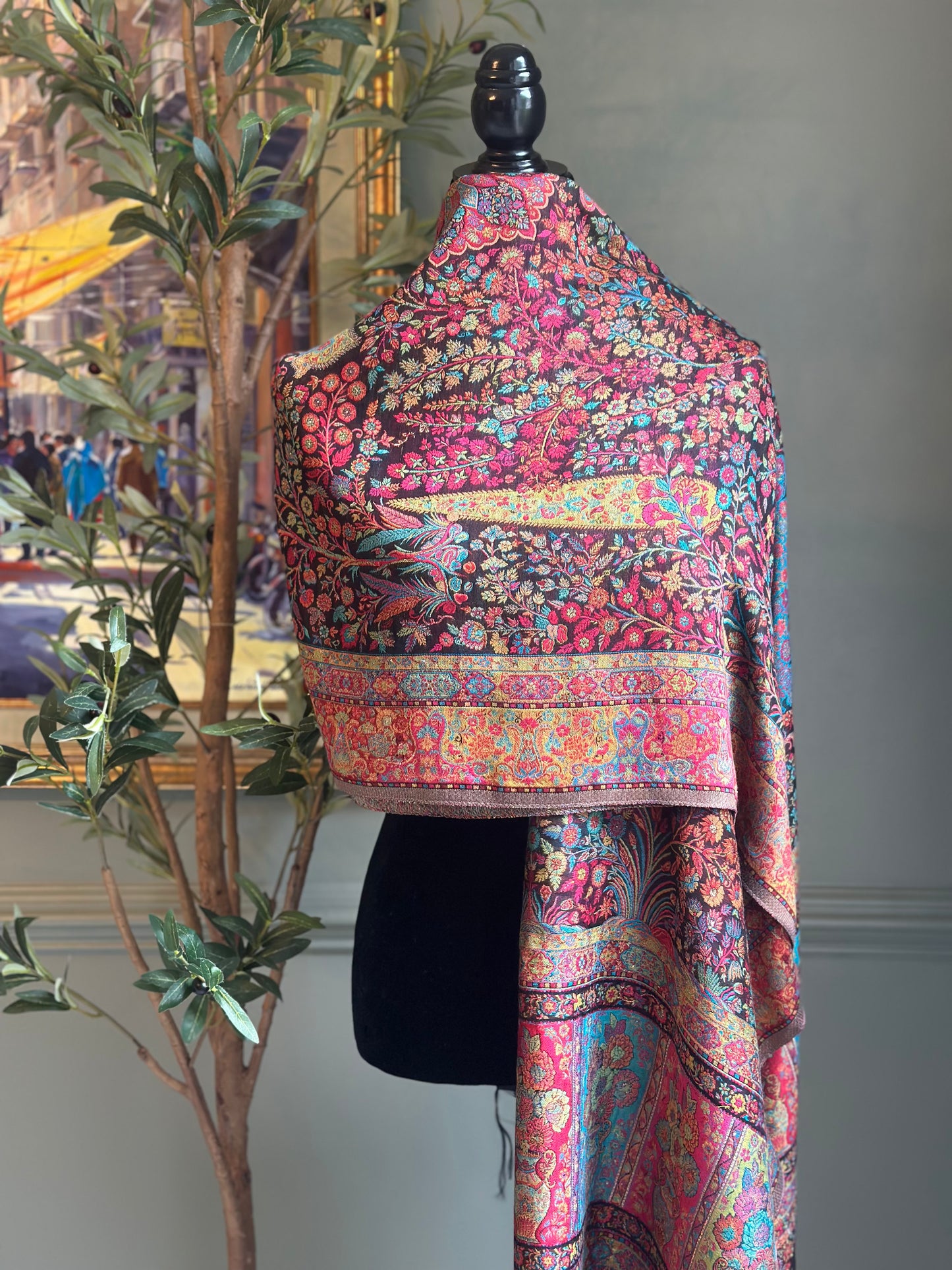 Colorful patterned wrap on a mannequin against a neutral wall with a plant in the background.