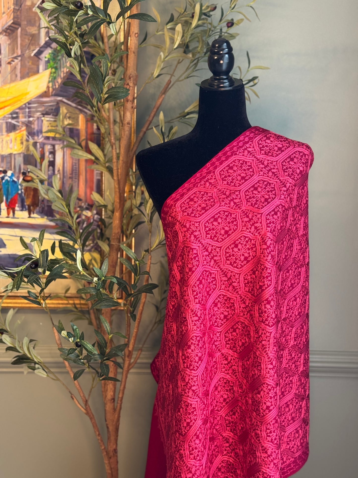 Mannequin wearing a bright pink patterned scarf with a cityscape painting and plant in the background