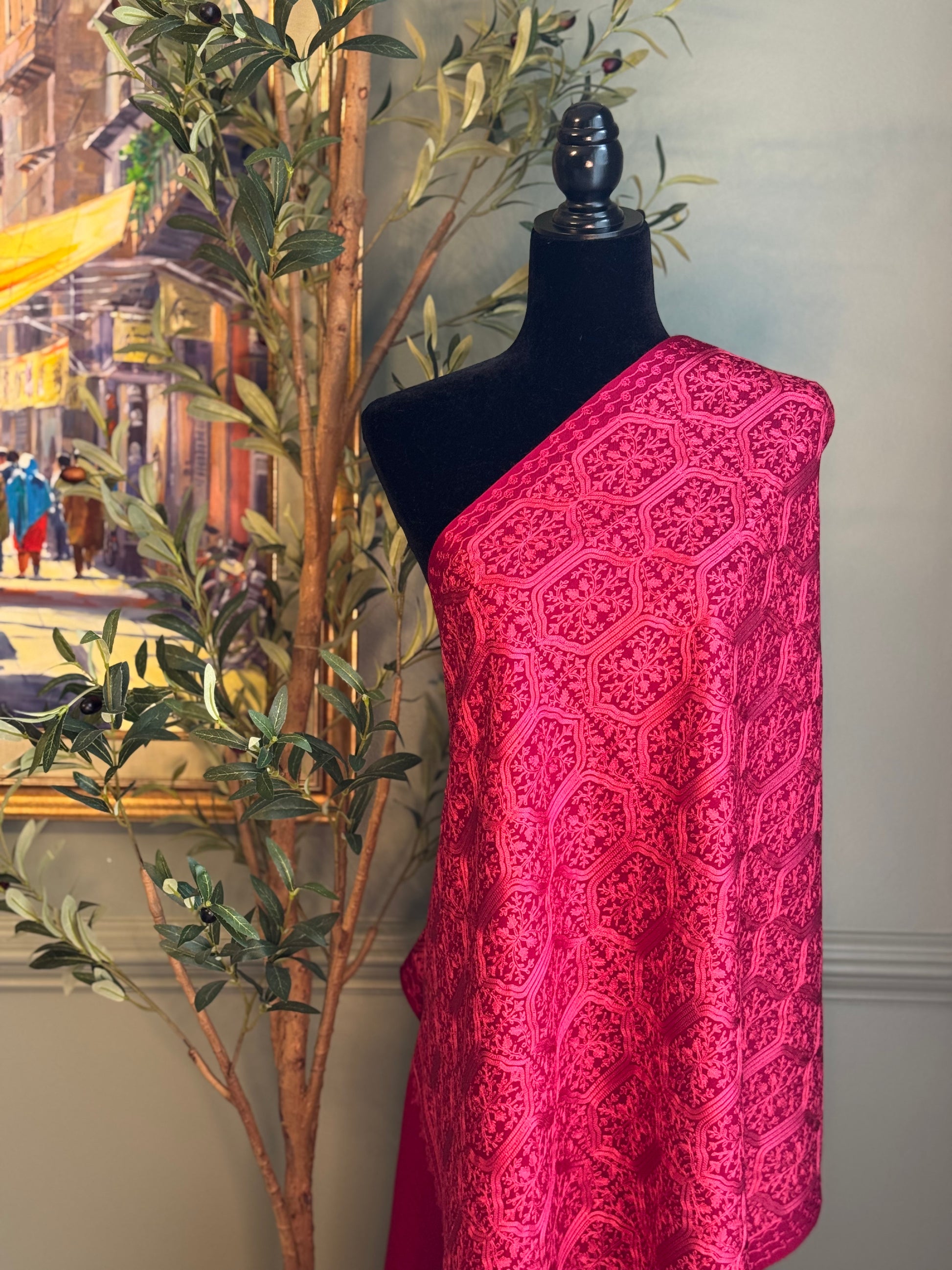 Mannequin wearing a bright pink patterned scarf with a cityscape painting and plant in the background